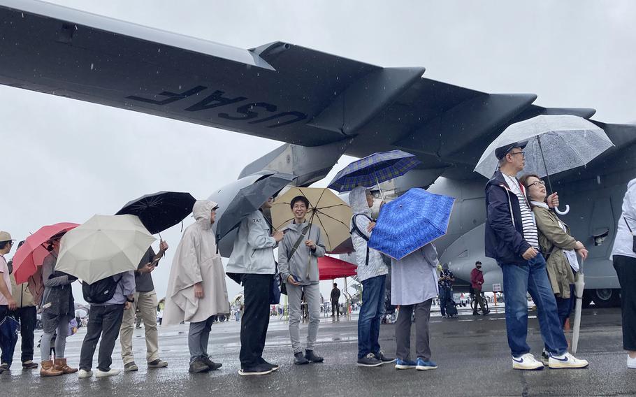 People with umbrellas line up on a rainy day with a C-17 in the background.