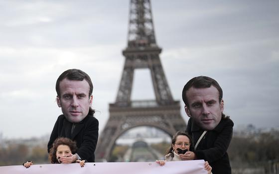 Gagged activists hold a placard as persons wearing a mask of French President Emmanuel Macron stand behind putting his hand on their mouth during a protest Friday, Nov. 24, 2023 in Paris. Activists say that France is vetoing a European decision on rape definition based on lack of consent. The large majority of EU member countries already treat violence against women and girls as a crime but the Commission said last year there are gaps in national legislation. (AP Photo/Christophe Ena)