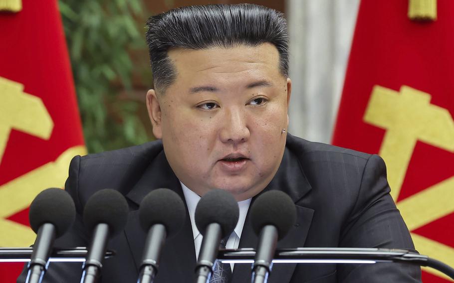 Kim Jong Un, wearing a black suit and seen from the chest up, speaks into a bank of five microphones.