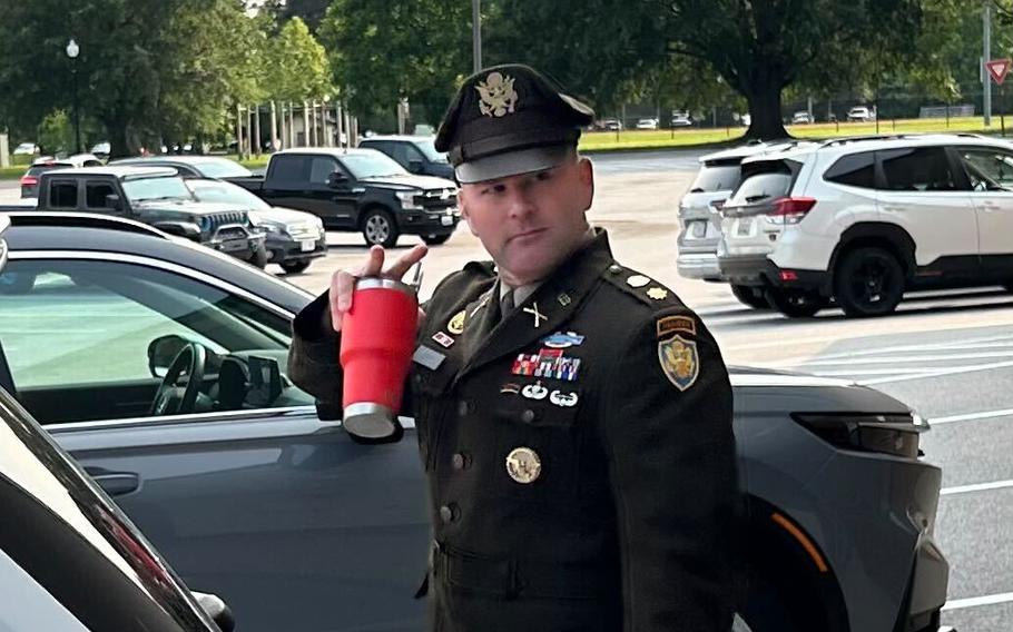 A soldier holds a red cup in a parking lot