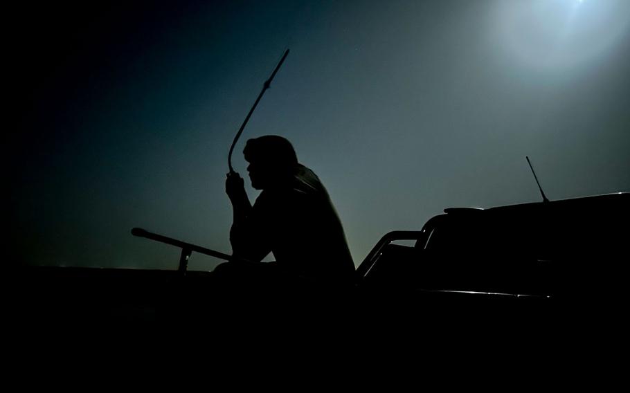 A service member in the shadows uses a radio.