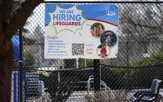A sign hanging on a fence says “We are hiring lifeguards.”