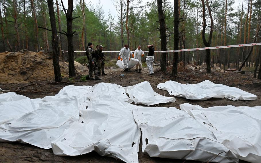Forensic technicians carry a body bag in a forest on the outskirts of Izyum, eastern Ukraine on Sept. 16, 2022. 