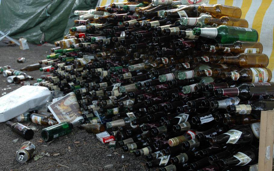 A large stack of opened and empty wine, beer and liquor bottles.