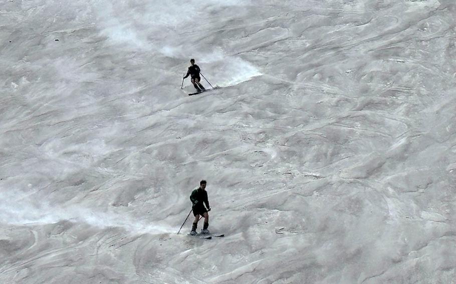 Two adults ski down a hill made of sand.