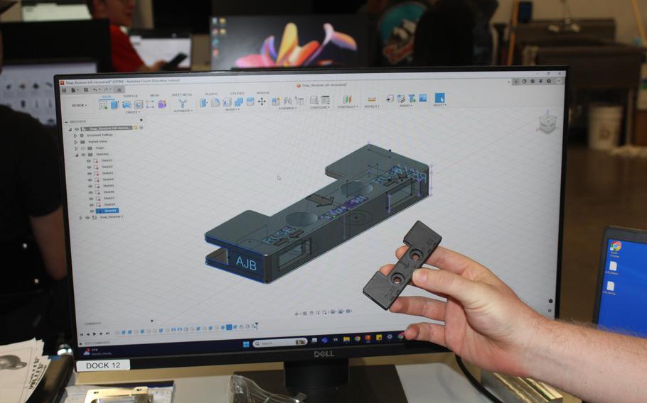 A hand holds a gray object in front of a computer screen displaying a representation of that object.