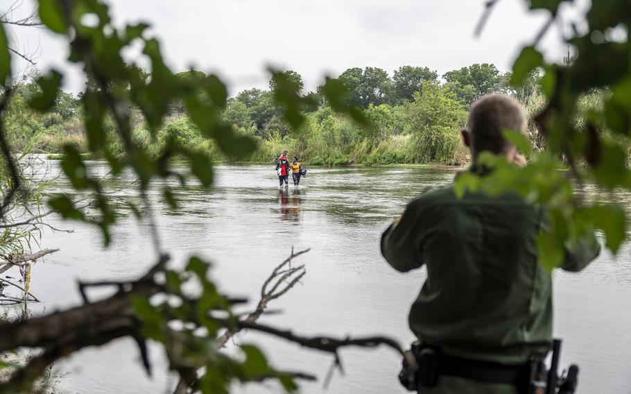 A Border Patrol agent watches a Haitian family approach the U.S. side of the Rio Grande on June 25 in Del Rio, Texas. MUST CREDIT: Photo for The Washington Post by Sergio Flores