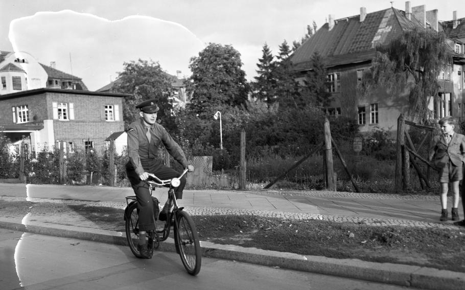 A black and white photo of a service member riding a bicycle on the left, while a boy on the right watches.