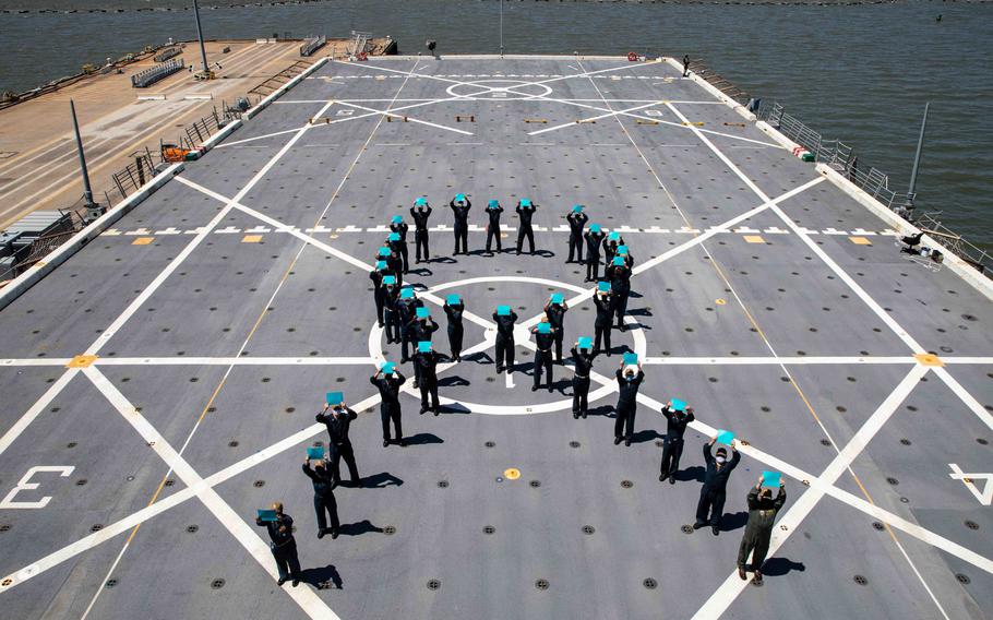 Sailors hold teal ribbons in formation on a ship.