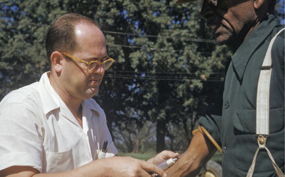 In this 1950s photo released by the National Archives, a Black man included in a syphilis study has blood drawn by a doctor in Tuskegee, Ala. 