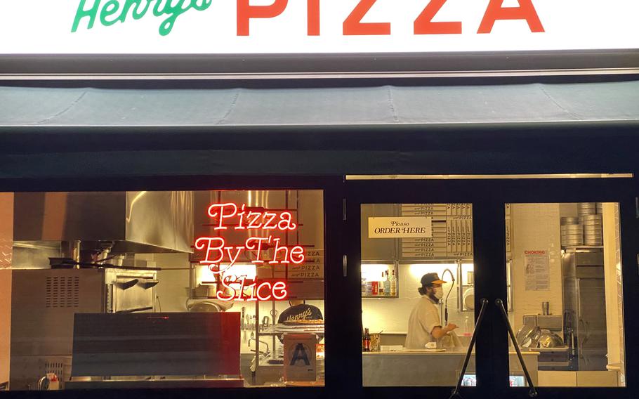 The exterior of Henry’s Pizza is lit up from within by a neon lettered sign and interior lights.