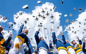 Air Force Academy graduates throw their caps into the air as jets fly overhead.