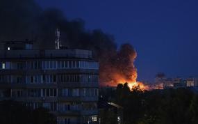 A fire burns behind some buildings at night.