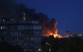 A fire burns behind some buildings at night.