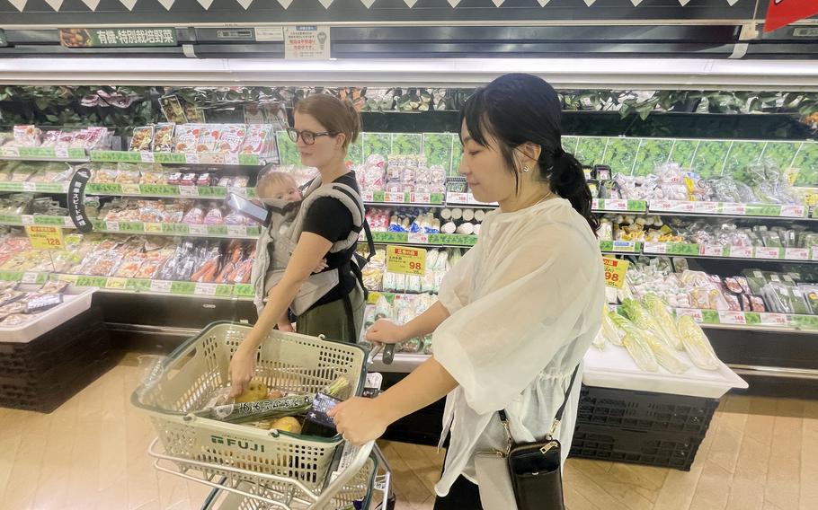 A member of the Japanese American Society shops with a Marine Corps spouse, who is carrying a baby, at a Japanese grocery store.