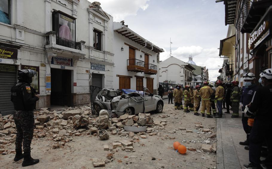 Rescue workers stand next to a car crushed by debris after an earthquake in Cuenca, Ecuador, Saturday, March 18, 2023.. The U.S. Geological Survey reported an earthquake with a magnitude of 6.7 about 50 miles south of Guayaquil.