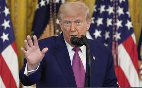 Trump gestures with his right hand while standing at a microphone.