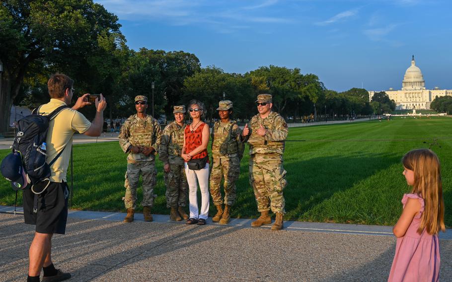 A woman and four Air National Guard members pose for a photo, all smiling, with the U.S. Capitol in the background.