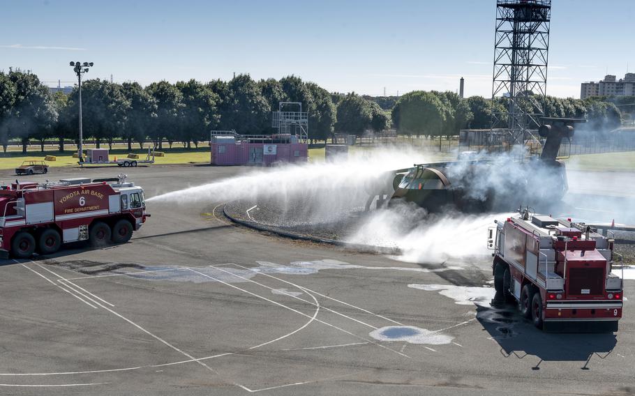 Military firetrucks spray water at a vehicle during a train exercise. 