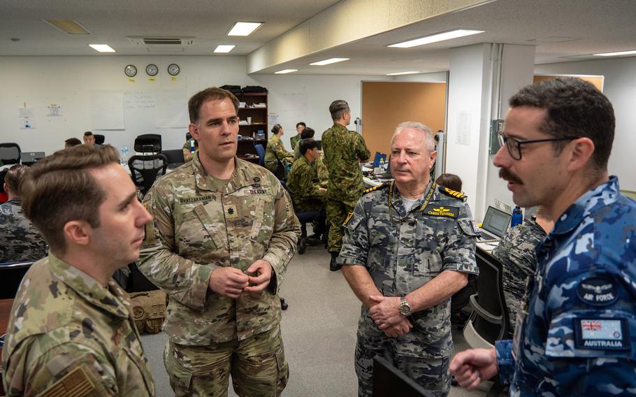 A group of military officers from different branches stand in discussion. Personnel wear various camouflage patterns including U.S. Army desert camouflage, digital camouflage and Australian Air Force blue camouflage.