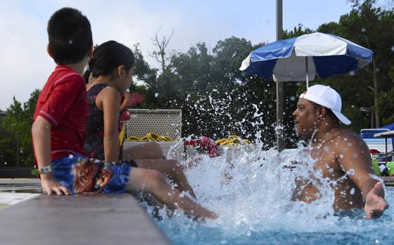 Children splash a man in an outdoor swimming pool.