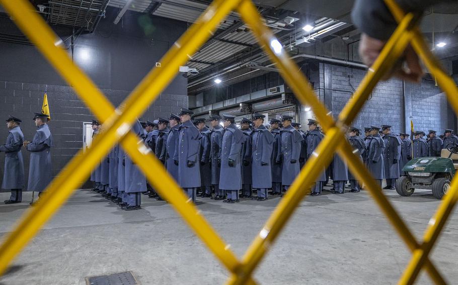 Cadets line up, seen through a yellow fence, before marching onto the field.