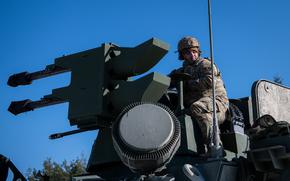 A soldier sits on a large piece of machinery.