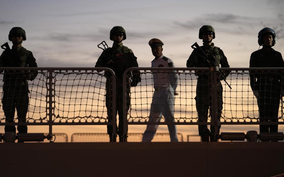 Sailors stand on deck, near the rail, with the sun rising behind them.