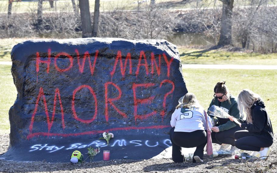 From left, Ella Huff, of Grand Rapids, joins fellow Michigan State University students Sophie Apple and her sister, Abbey Apple, both of Washington Township, as they place flowers at ‘The Rock,’ Tuesday morning, Feb. 14, 2023.