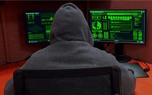 An image of a man in a hoodie looking at two computer monitors with green displays, against a red background.