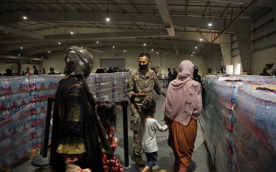 Sgt. Juan Miranda, culinary specialist, 155th Combat Sustainment Support Battalion, directs Afghan evacuees into the dining facility at Camp As Sayliyah, Qatar, Aug. 20, 2021. Soldiers provide meals, water, and snacks to Special Immigration Visa applicants seeking relocation to the United States. 