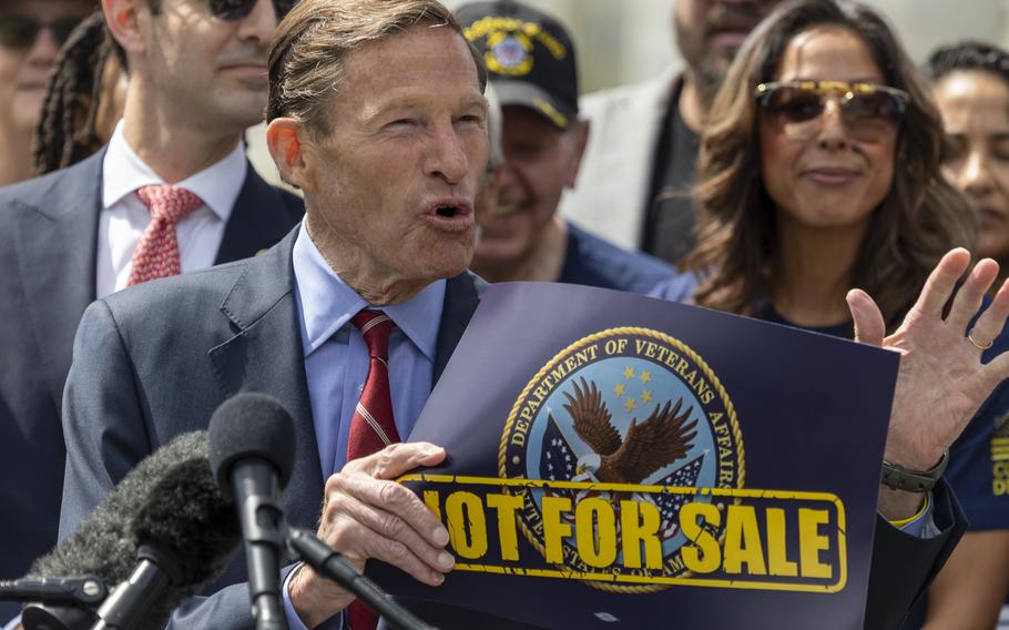Richard Blumenthal speaks into a microphone while standing in front of rally-goers and holding a poster with the VA emblem and the words “Not For Sale.”