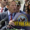 Richard Blumenthal speaks into a microphone while standing in front of rally-goers and holding a poster with the VA emblem and the words “Not For Sale.”