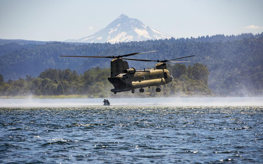 Army National Guard and Reserve members stand on the shore of a lake with a helicopter in the foreground.