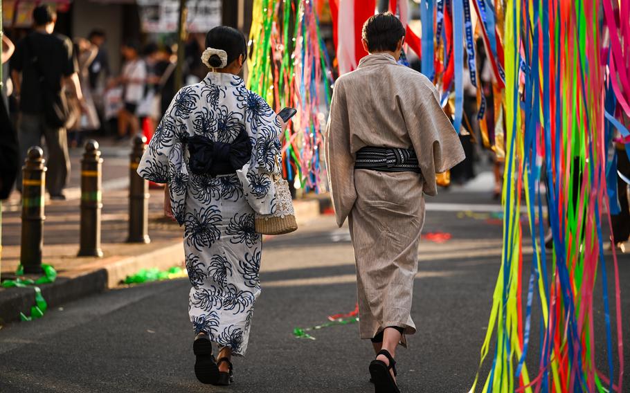 Festival goers in traditional Japanese yukata walk through streamers and paper strips at the Tanabata Festival in Fussa, Japan, Aug. 8, 2025.