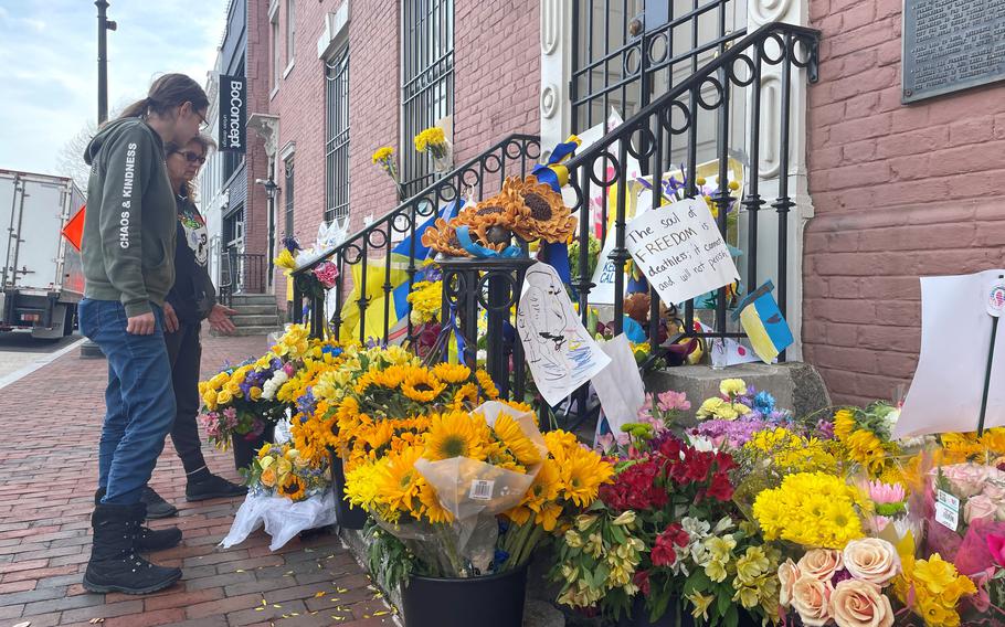 Emily Lowe waits outside the Ukrainian Embassy in Washington as her fiance goes inside to volunteer to join the war. His mother, Sandi Simpson, looks at the flowers next to her. 
