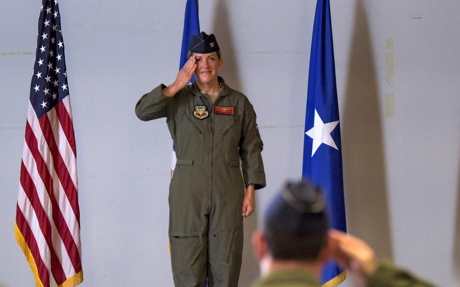 Woman stands at attention and renders a salute to other troops.