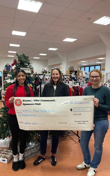 Three women holding up a giant check under indoor lights