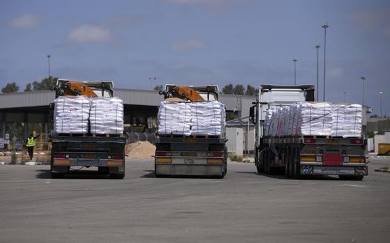 Three flat-bed trucks loaded with humanitarian supplies, seen from behind, wait at a border crossing terminal.
