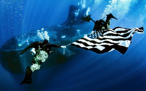 Military members from Naval Special Warfare Group Eight display the national ensign as they perform dive operations while underway on a Virginia Class fast-attack submarine USS New Mexico (SSN 778) in June 2022. The Naval Special Warfare groups specialize in a broad range of tactical areas, including unconventional warfare, direct action, counterterrorism, special reconnaissance and personnel recovery.