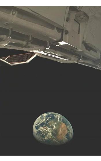 A vertical photo of the Earth seen from space, with the Earth at the bottom and parts of a spacecraft at the top.