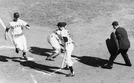 Bobbby Thomson (left) of the New York Giants scores a run in the second inning of game three of the World Series in New York, Oct. 6, 1951. New York Yankees catcher Yogi Berra (obscured, second left) crouches to catch the ball as an unidentified Giant steps up to bat and the umpire watches the action. The Yankees won the game and went on to win the series. 