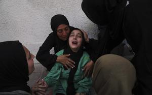 A woman mourns as other women hold and surround her.