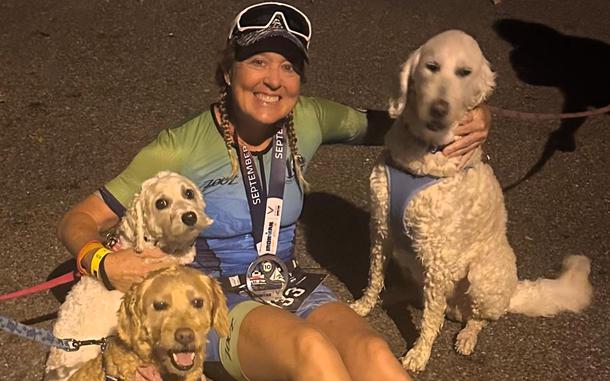 A woman poses with three dogs in her Ironman triathlon attire. 