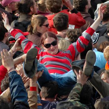A concert-goer in a striped shirt or sweater and blue jeans crowd surfs.