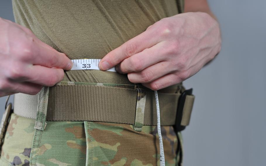 An individual wearing fatigues measuring his waist line.