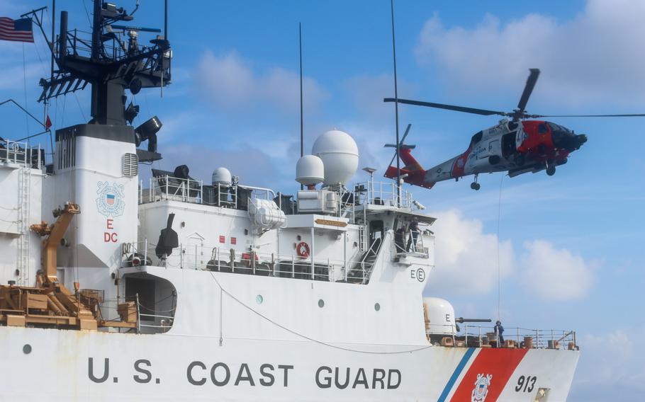 A helicopter flies over a Coast Guard cutter.