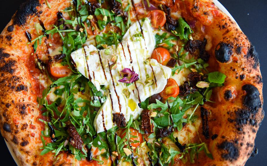 A pizza topped with burrata sits on a dish, ready to be eaten.
