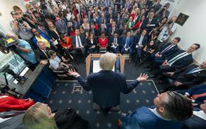 Reporters listen as the president, with his back to the camera, answers questions.