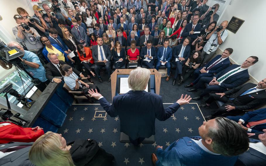 Reporters listen as the president, with his back to the camera, answers questions.